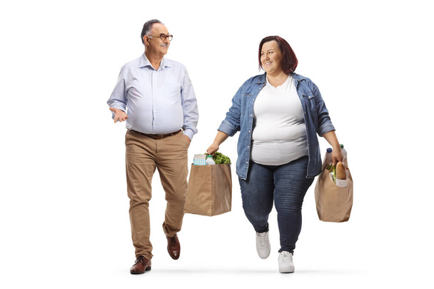 Overweight woman carrying grocery bags walking and talking to a mature man isolated on white background - Фото, изображение