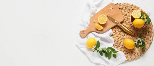 Bowl and cutting board with knife, fresh lemons and blooming branches on white background with space for text - Photo, Image