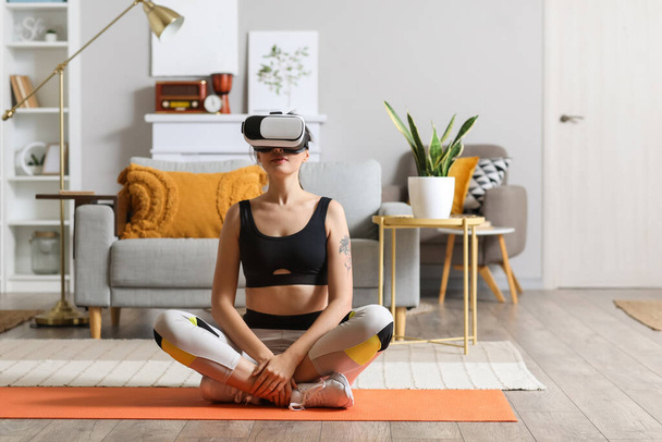Sporty young woman in VR glasses  meditating at home - Фото, зображення