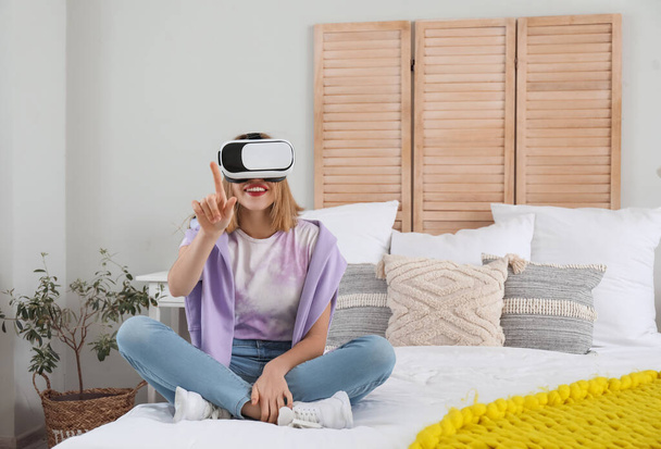 mooie jonge vrouw in VR bril in slaapkamer - Foto, afbeelding