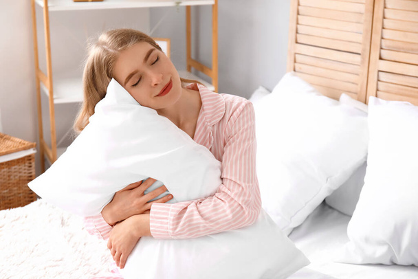 Młoda kobieta z miękką poduszką siedzi w sypialni - Zdjęcie, obraz