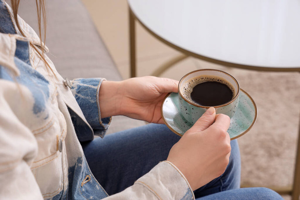 Kobieta siedzi na kanapie i trzyma filiżankę pysznej kawy - Zdjęcie, obraz