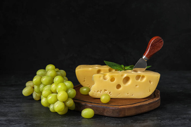Board with tasty Swiss cheese and grapes on black background - 写真・画像