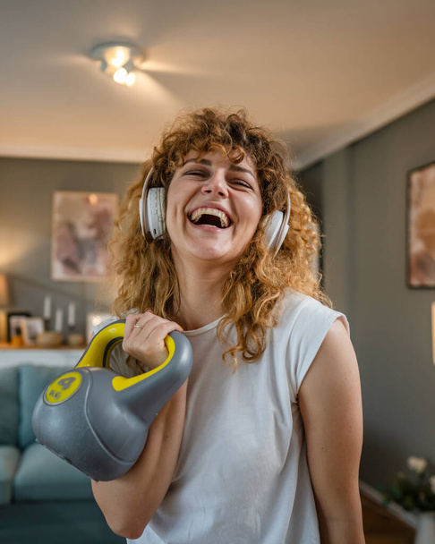 portrait of caucasian adult woman with curly hair stand at home hold kettlebell girya wear white t-shirt before or after training healthy lifestyle concept copy space - Photo, Image
