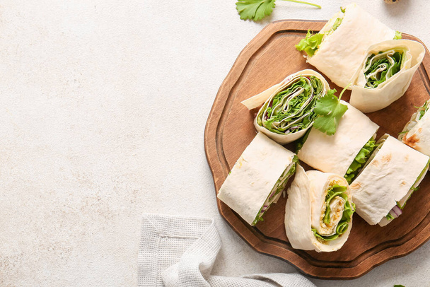 Wooden board of tasty lavash rolls with onion, egg and greens on light background - Foto, immagini