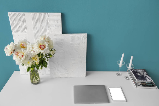 Ваза с белыми пионами и картинами на столе у голубой стены - Фото, изображение