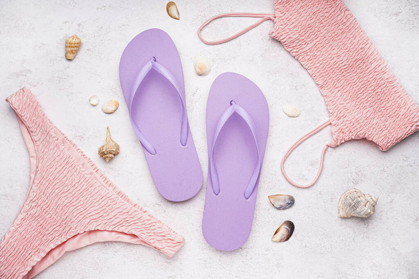 Lilac flip-flops with swimsuit and shells on white grunge background - Фото, изображение