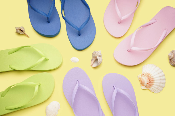 Different color flip-flops with shells on yellow background - Zdjęcie, obraz