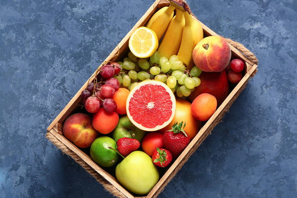 Caixa de madeira com diferentes frutas frescas no fundo azul - Foto, Imagem