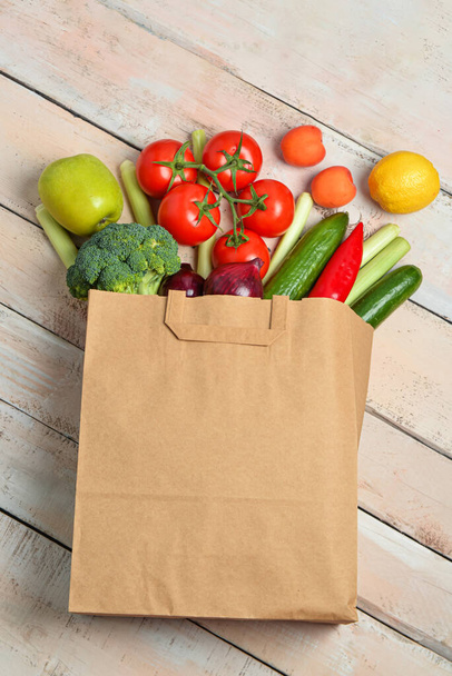 Bolsa de papel con verduras y frutas frescas sobre fondo de madera clara - Foto, Imagen