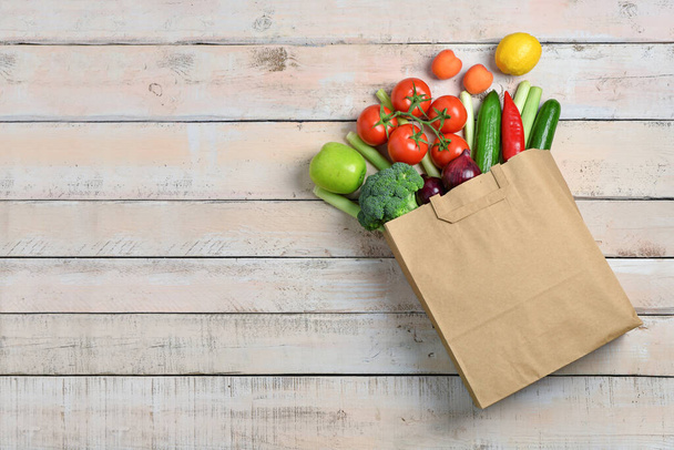 Paper bag with fresh vegetables and fruits on light wooden background - Фото, зображення