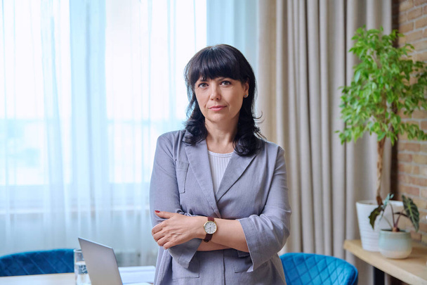 Portrait of a beautiful mature business woman with crossed arms in office. Confident smiling 50 year old female looking at the camera. Age, beauty, business, work concept - Valokuva, kuva
