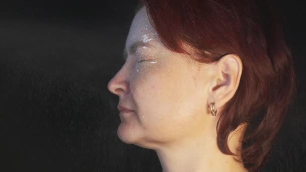 Una mujer con el pelo corto rojo espolvorea espuma blanca en su cara para el rejuvenecimiento. Vídeo horizontal 4K. Imágenes cinematográficas - Metraje, vídeo