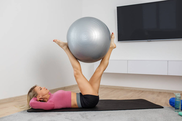 Millennial nainen käyttää kunto pallo liikunta matto olohuoneessa. Kunto, urheilu ja terveelliset elämäntavat. - Valokuva, kuva
