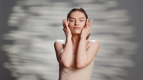 Confident woman using moisturizing facial cream for beauty routine, creating new ad campaign for glowing products. Cheerful sensual girl posing on camera to advertise nourishing luminous look. - 写真・画像