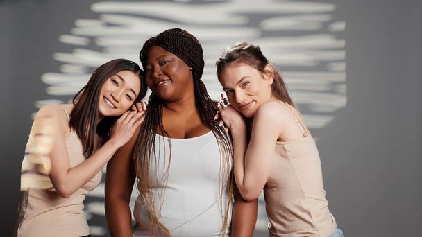 Gruppe multiethnischer Frauen, die für Körperpositivitätsanzeige lächeln, kurvige und magere Freundinnen, die für Weiblichkeit und Körperbewusstsein werben. Mädchen mit unterschiedlichen Hautfarben und Körpertypen im Studio. - Foto, Bild