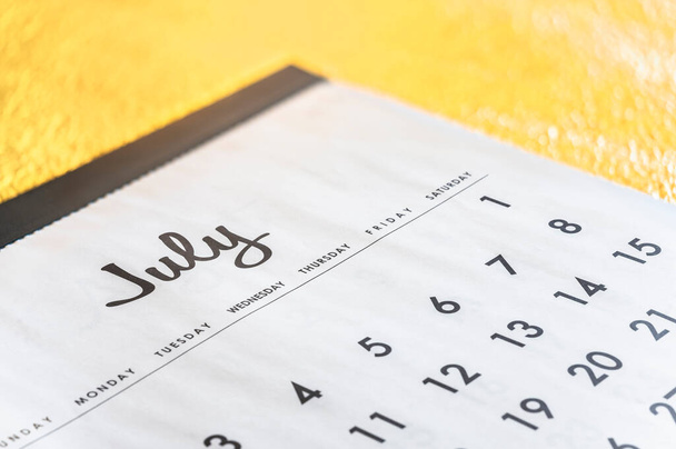 Detailed close-up of a straightforward calendar specifically focusing on the month of July with the days of the week written in English set against a golden backdrop with a shallow depth of field. - Фото, зображення