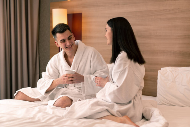 young couple on honeymoon in hotel room having breakfast room drinking coffee happy lovers travel concept - Photo, Image