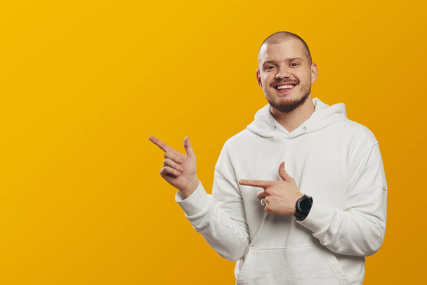 Cheerful man points aside on empty space with both hands, advertises copy space for your advertising content, isolated over yellow background - Foto, Bild