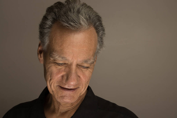Portrait of a mature man with graying hair wearing a black shirt 60plus looking down - Photo, Image