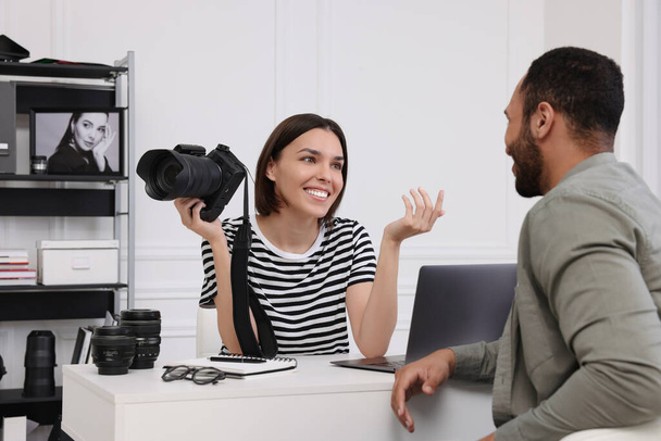 Young professional photographer holding camera while talking with man in modern photo studio - Foto, immagini