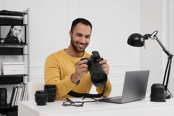 Young professional photographer with camera at table in modern photo studio - Valokuva, kuva