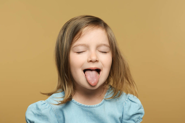 Funny little girl showing her tongue on beige background - 写真・画像