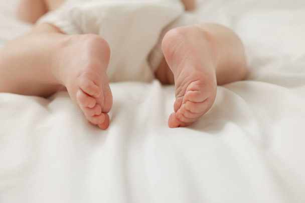 Little baby in diaper on white bed, closeup - Foto, Bild