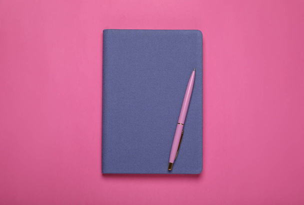 Blue office notebook and pen on pink background, top view - Foto, afbeelding
