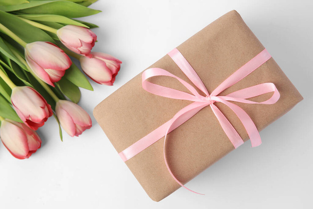 Beautiful gift box with bow and pink tulips on white background, flat lay - Fotografie, Obrázek