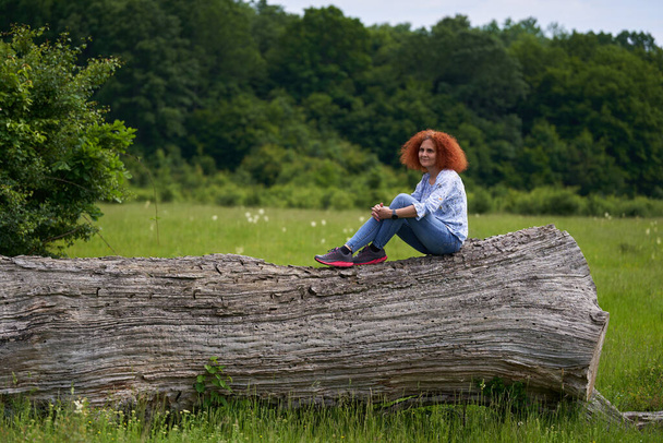 Portrait of a redhead curly hair woman on a meadow in an oak forest - Foto, afbeelding