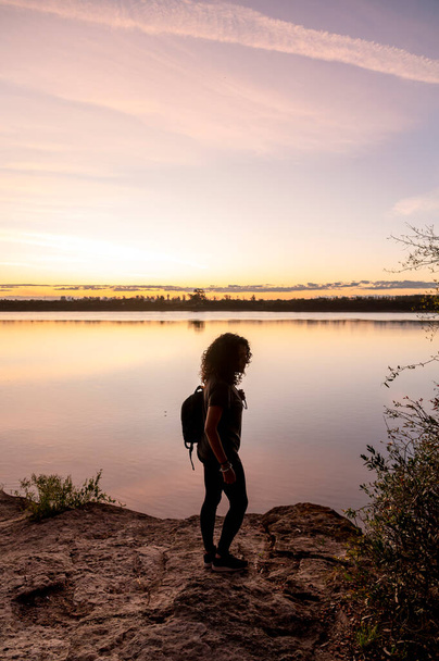 Gün batımında göl kenarında yürüyen gezgin kadın. Doğa ve seyahat kavramı. - Fotoğraf, Görsel