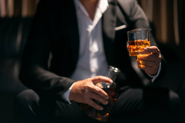 İş adamı içki deposunda elinde viski bardağıyla oturuyor. - Fotoğraf, Görsel