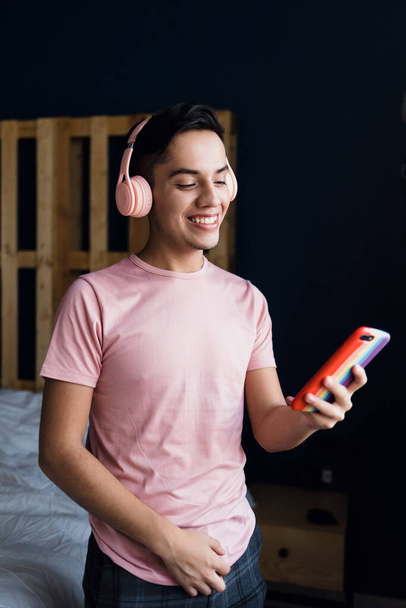 giovane uomo omosessuale latino con cuffie ascoltare musica sul cellulare a casa in Messico, comunità ispanica LGBT in America Latina - Foto, immagini