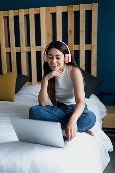 Latin Amerika 'da Latin kökenli Latin kökenli genç bir kız öğrenci, evinde yatağında dizüstü bilgisayar ve kulaklık kullanıyor. - Fotoğraf, Görsel
