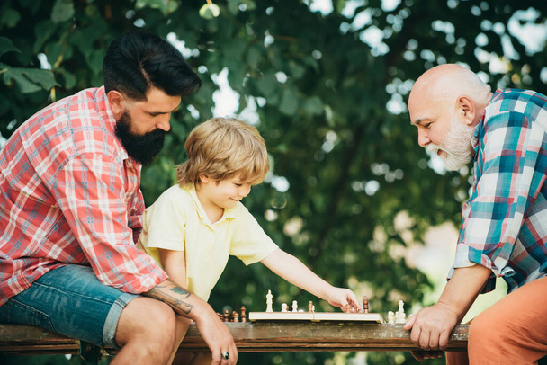 Concept of Fathers day. Senior man teaching his grandson to play chess. Happy man family concept playing Chess and have fun together - Φωτογραφία, εικόνα