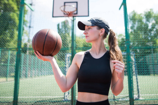 Young sports girl with a basketball on the basketball court outdoors, active weekend. - Foto, Bild