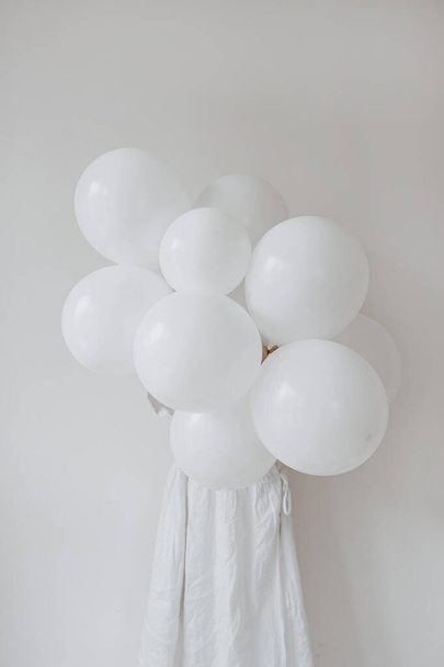 Woman in white dress holding bunch of birthday balloons over white background. Festive holiday event party celebration concept. Party time - Fotó, kép