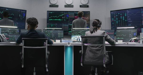 Multi ethnic team of traders work on multi-monitor computers with displayed real-time stocks. Colleagues analyze exchange market charts on big screens. Cryptocurrency trading and investment. Zoom out. - Photo, Image