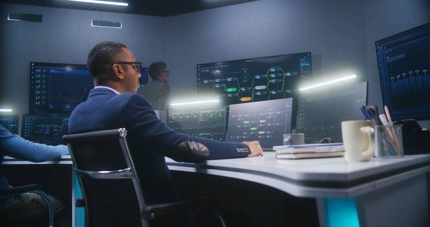 Multiethnische IT-Techniker sitzen in Überwachungsbüros vor Computern mit Datenserver. Software-Ingenieur arbeitet mit Live-Analyse-Diagrammen und Blockchain-Netzwerk auf großen digitalen Bildschirmen. - Foto, Bild