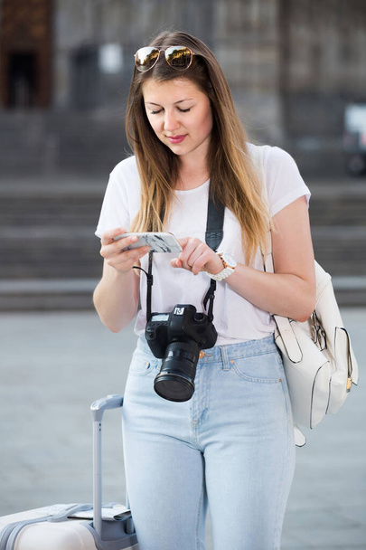Young cheerful american traveling girl searching for the direction using her phone in the town . - 写真・画像