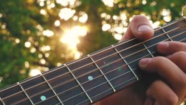 Παίζω κιθάρα στο ηλιοβασίλεμα. Ηλιαχτίδες σε χορδές κιθάρας. Μουσική ακούγεται σε χορδές κιθάρας - Πλάνα, βίντεο