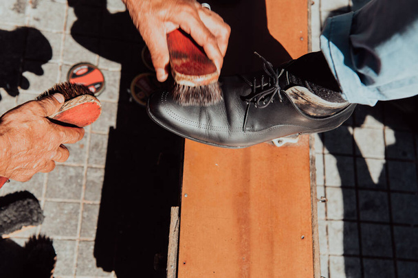 Een oude man hand polijsten en schilderen van een zwarte schoen op straat. - Foto, afbeelding