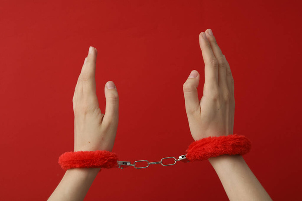 Red fluffy handcuffs on the hands on a red background - Photo, Image