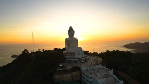 Великий Будда на заході сонця з дрона. Фантазія. Люди піднімаються сходами до статуї. Зелені пагорби острова навколо. Вдалечині яскраве сонце сідає над морем. Вид згори - Фото, зображення
