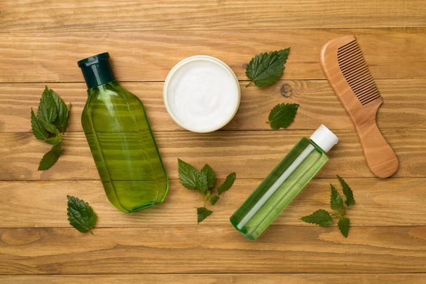 Shampoo and hair mask with nettle extract on wooden background, top view - Фото, изображение