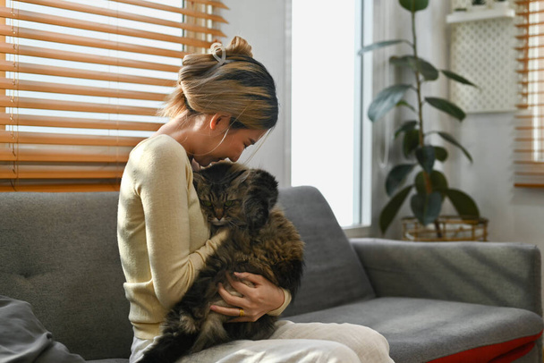 Liefdevolle jonge vrouw die thuis speelt met haar pluizige kat. Het concept van mens, huisdier en levensstijl. - Foto, afbeelding