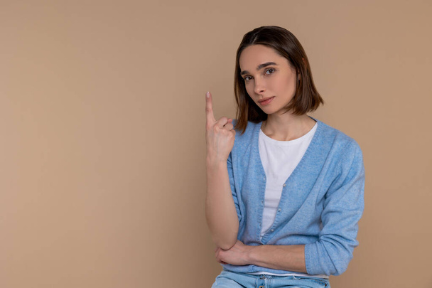 Attractive woman in casual clothing showing number one with finger isolated over beige background. - Фото, зображення