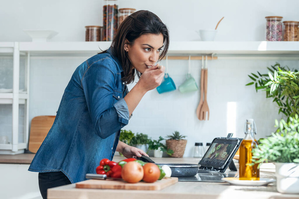 Shot of beautiful young woman cooking healthy food and using digital tablet to recipes in the kitchen at home. - Foto, Bild
