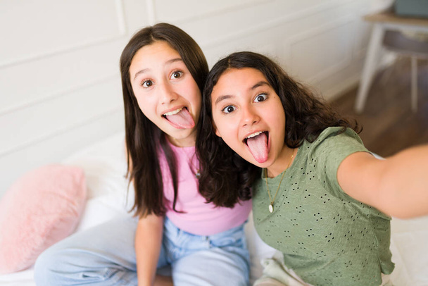 Alegre adolescentes y mejores amigas sacando la lengua y haciendo caras divertidas mientras se toman selfies juntos  - Foto, imagen